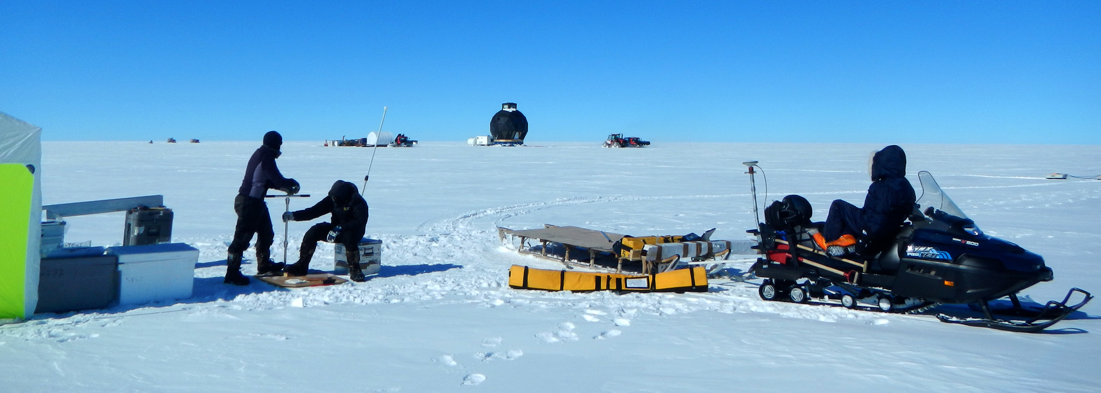 Helle and Paul are taking snow samples, while Anna is watching the traverse train go by. To the right the snowmobile with radar equipment is seen